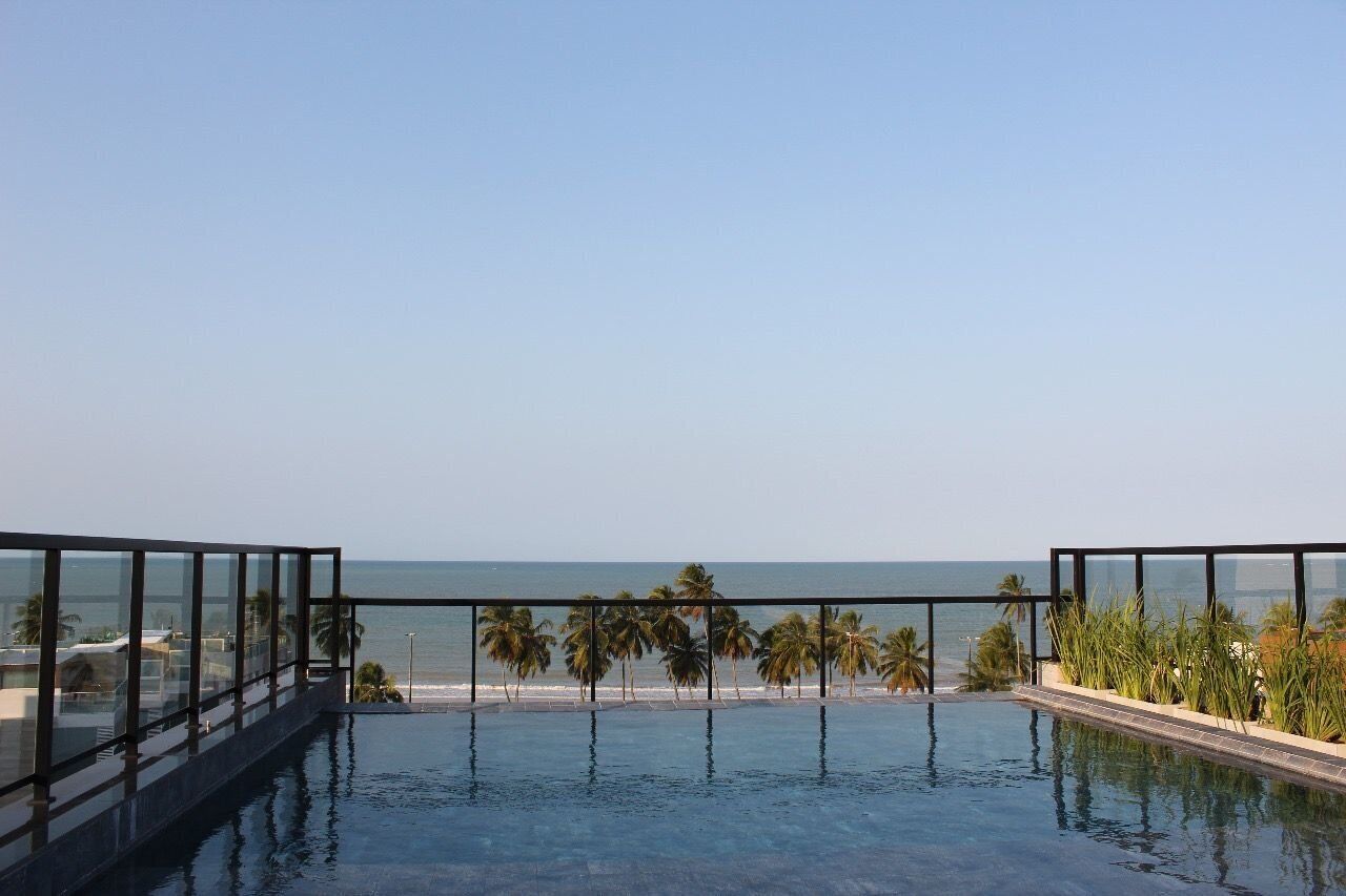 Piscina infinita no terraço com vista para o oceano e palmeiras.