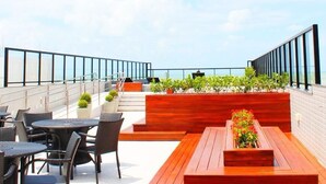 Een dakterras met buitenmeubels, een houten plantenbak met bloemen en uitzicht op de oceaan.