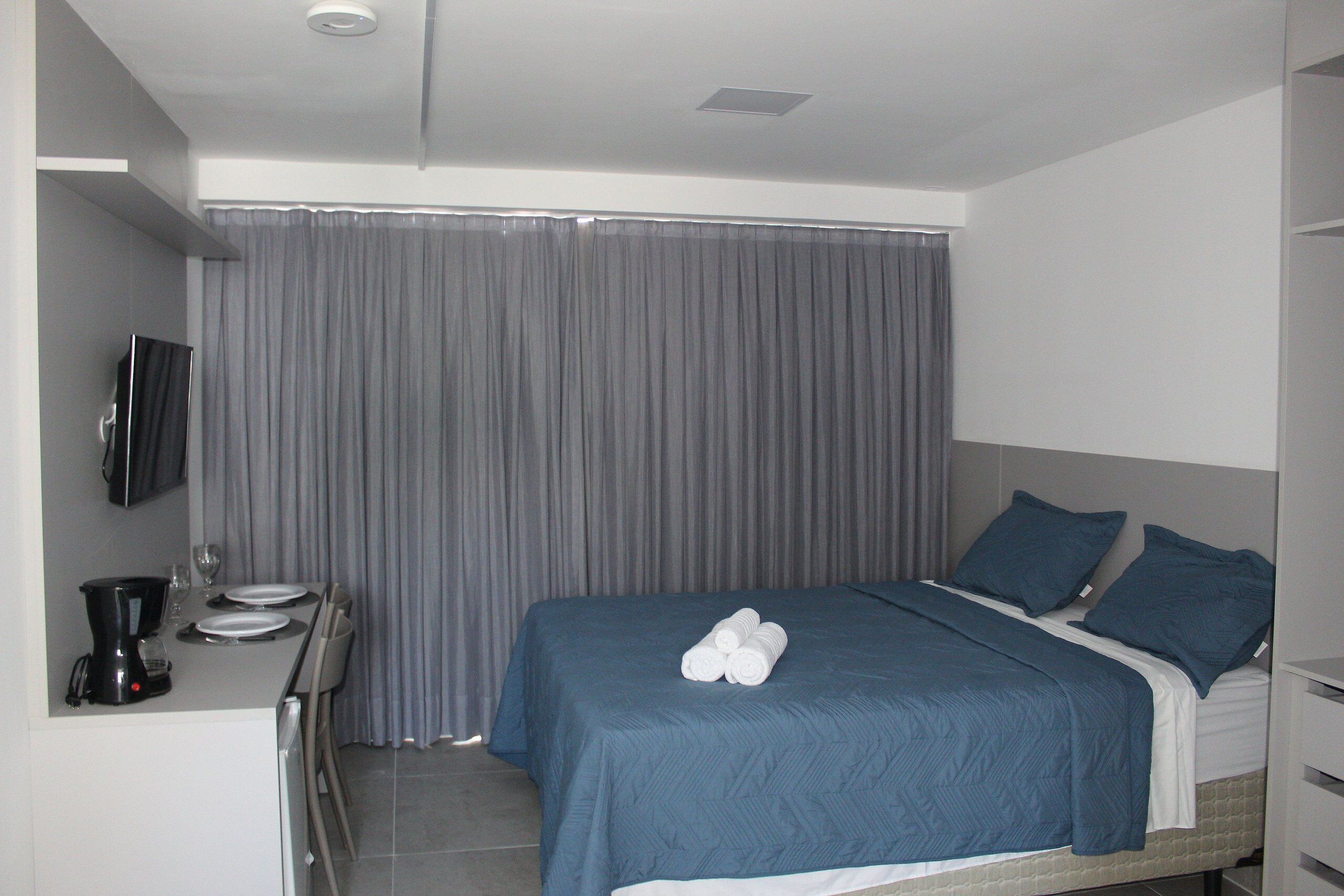 A hotel room with a bed, a desk with a coffee maker, and a TV mounted on the wall.