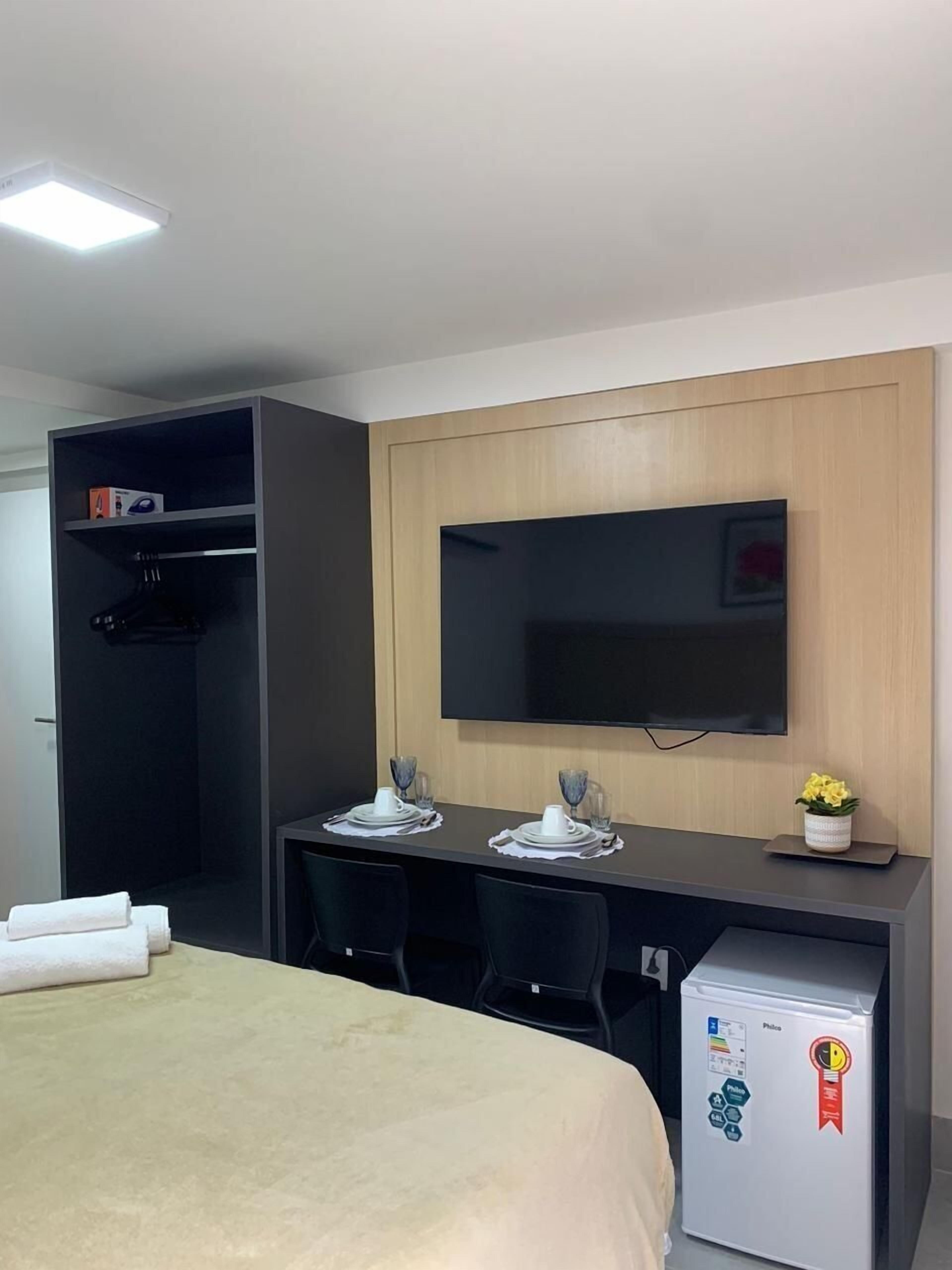 Ein Hotelzimmer mit einem Bett, einem Schreibtisch mit zwei Stühlen, einem an der Wand befestigten Fernseher und einer Minibar.