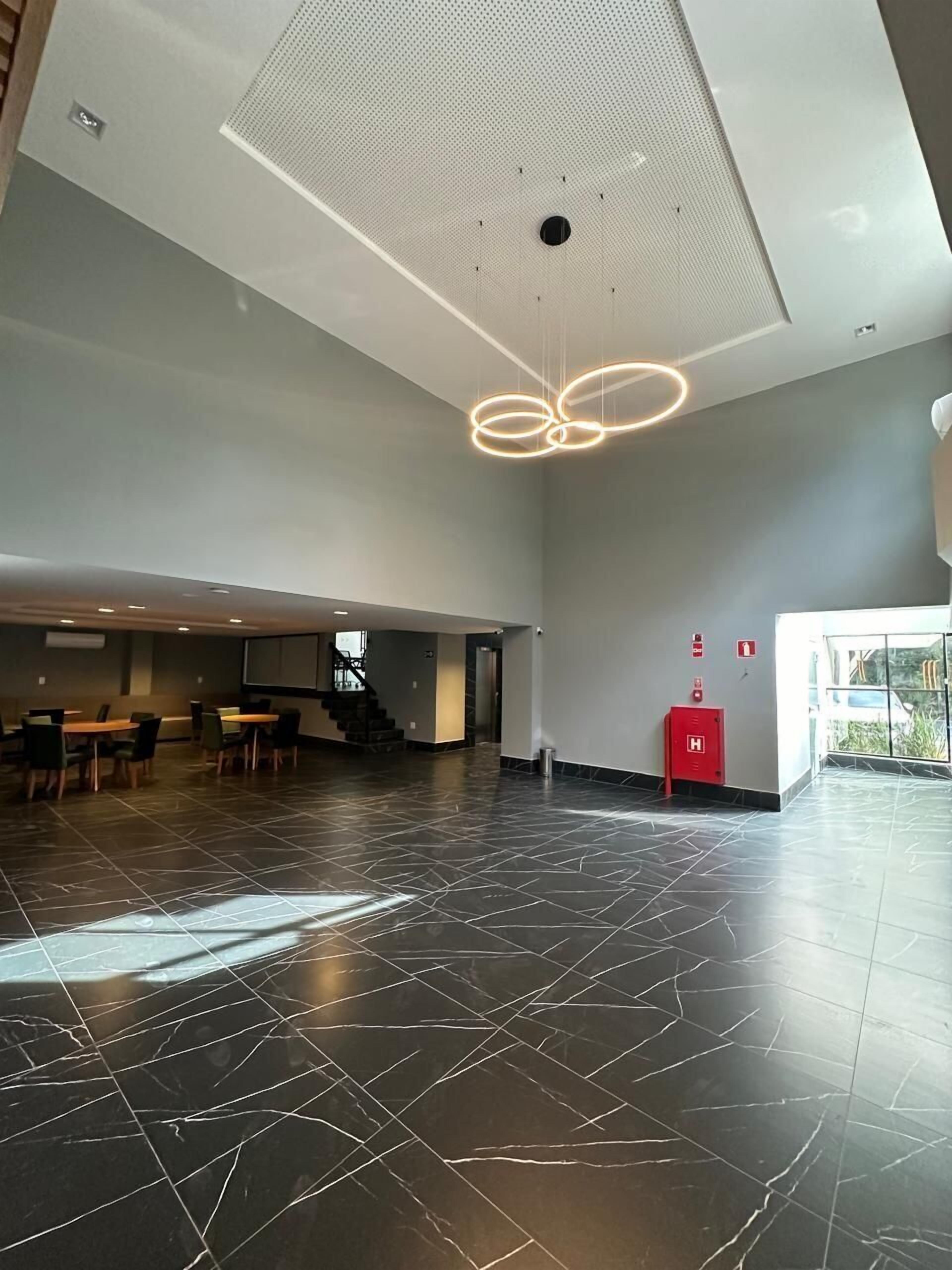 A spacious lobby with a modern design, featuring a large open area with a patterned floor, a seating area with tables and chairs, and a ceiling with a unique light fixture.