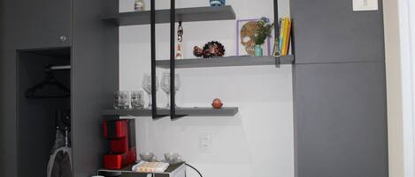 A compact kitchen with a microwave, coffee maker, and shelves with decorative items.