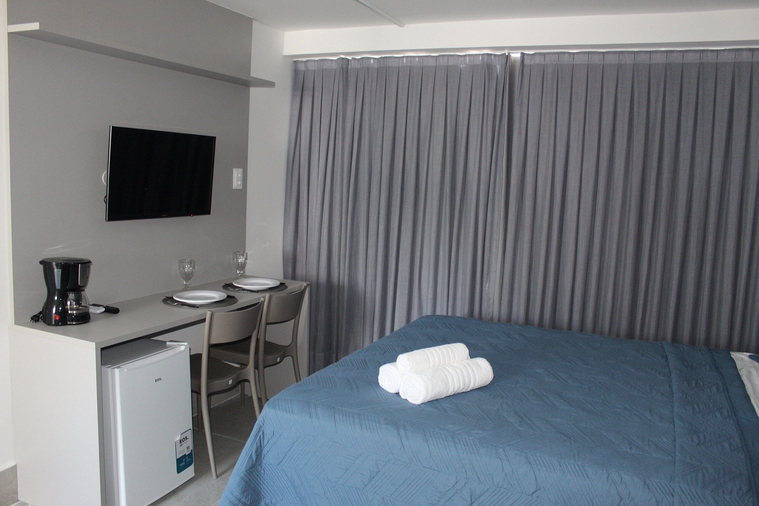 A hotel room with a bed, a desk with a coffee maker, a television, and a dining table with chairs.
