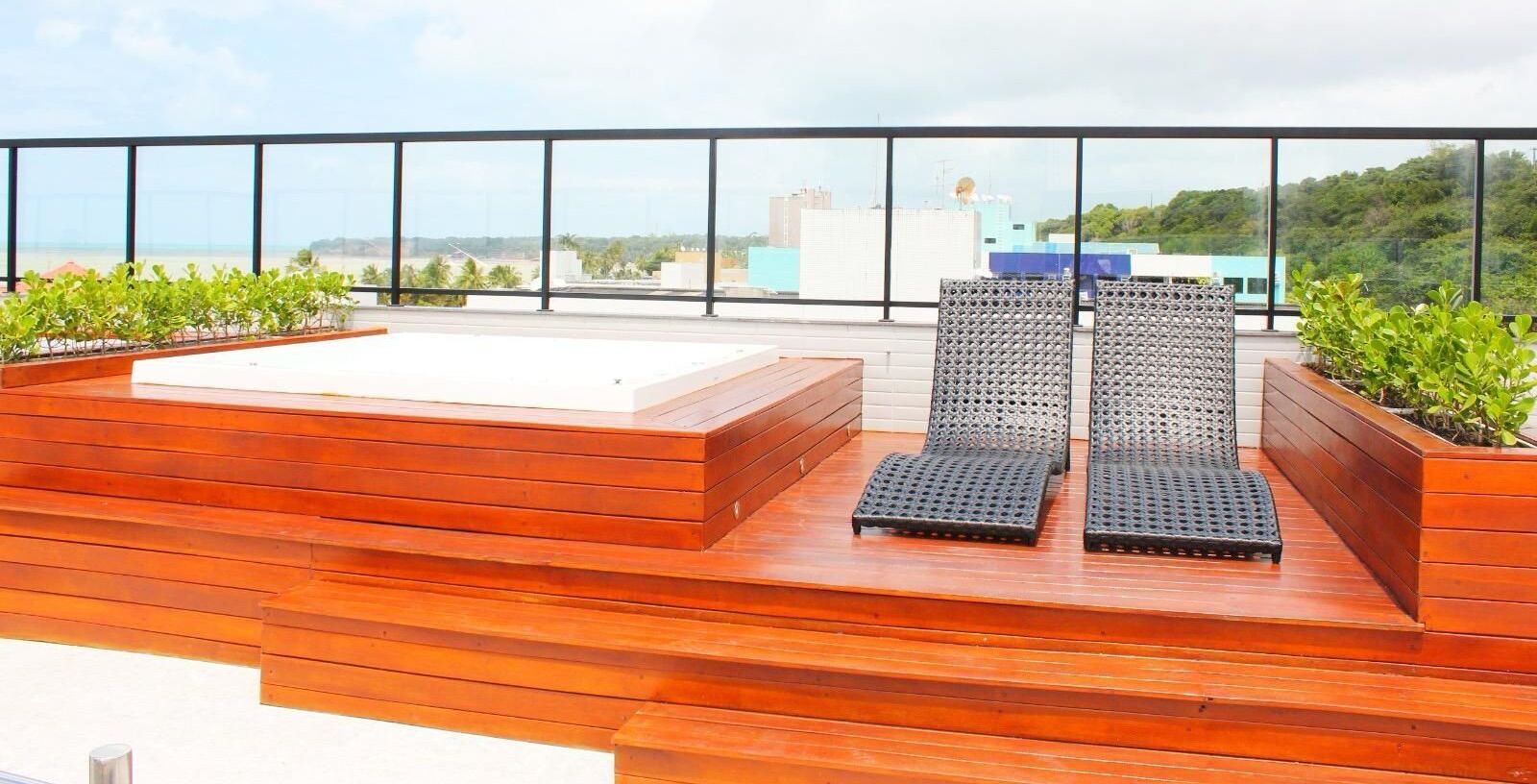 A rooftop terrace with wooden flooring, two lounge chairs, and a small white table.