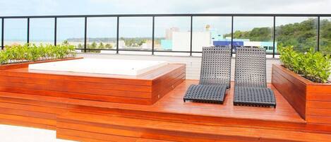 A rooftop terrace with wooden flooring, two lounge chairs, and a small white table.