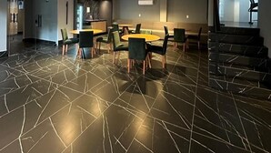 Een ruime kamer met een modern design, met een marmeren vloer, een centrale eettafel met stoelen en een trap naar een hoger niveau.