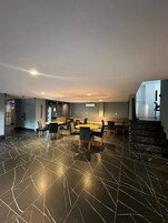 Um quarto espaçoso com design moderno, apresentando piso de mármore, uma mesa de jantar central com cadeiras e uma escadaria para um andar superior.