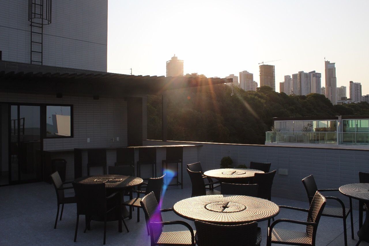 Un patio en la azotea con mesas y sillas redondas, un horizonte urbano al fondo y cielo despejado.