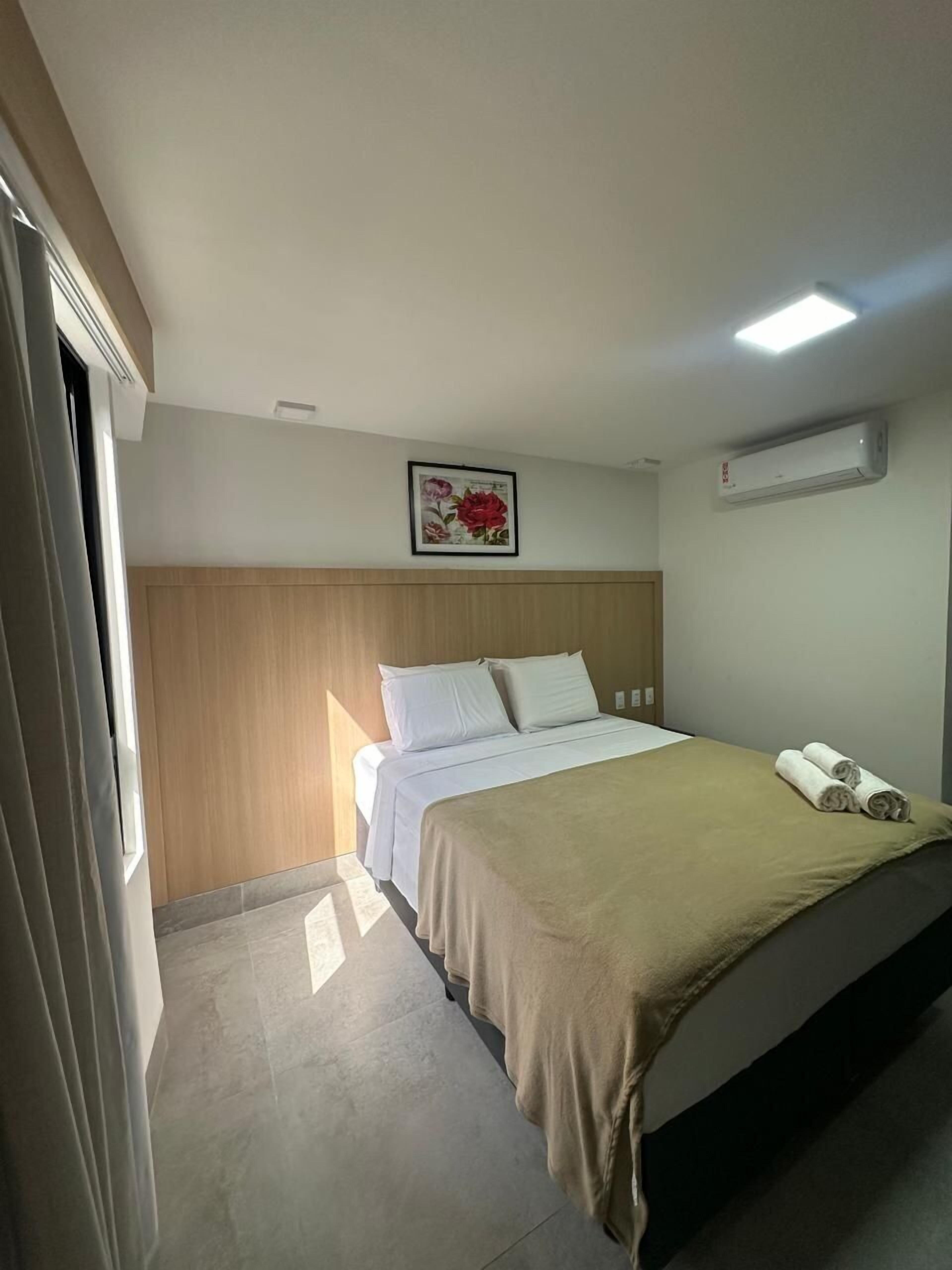 Een hotelkamer met een bed, een wandairconditioner en een bloemrijk kunstwerk in een lijst boven het bed.