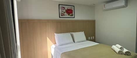 Een hotelkamer met een bed, een wandairconditioner en een bloemrijk kunstwerk in een lijst boven het bed.