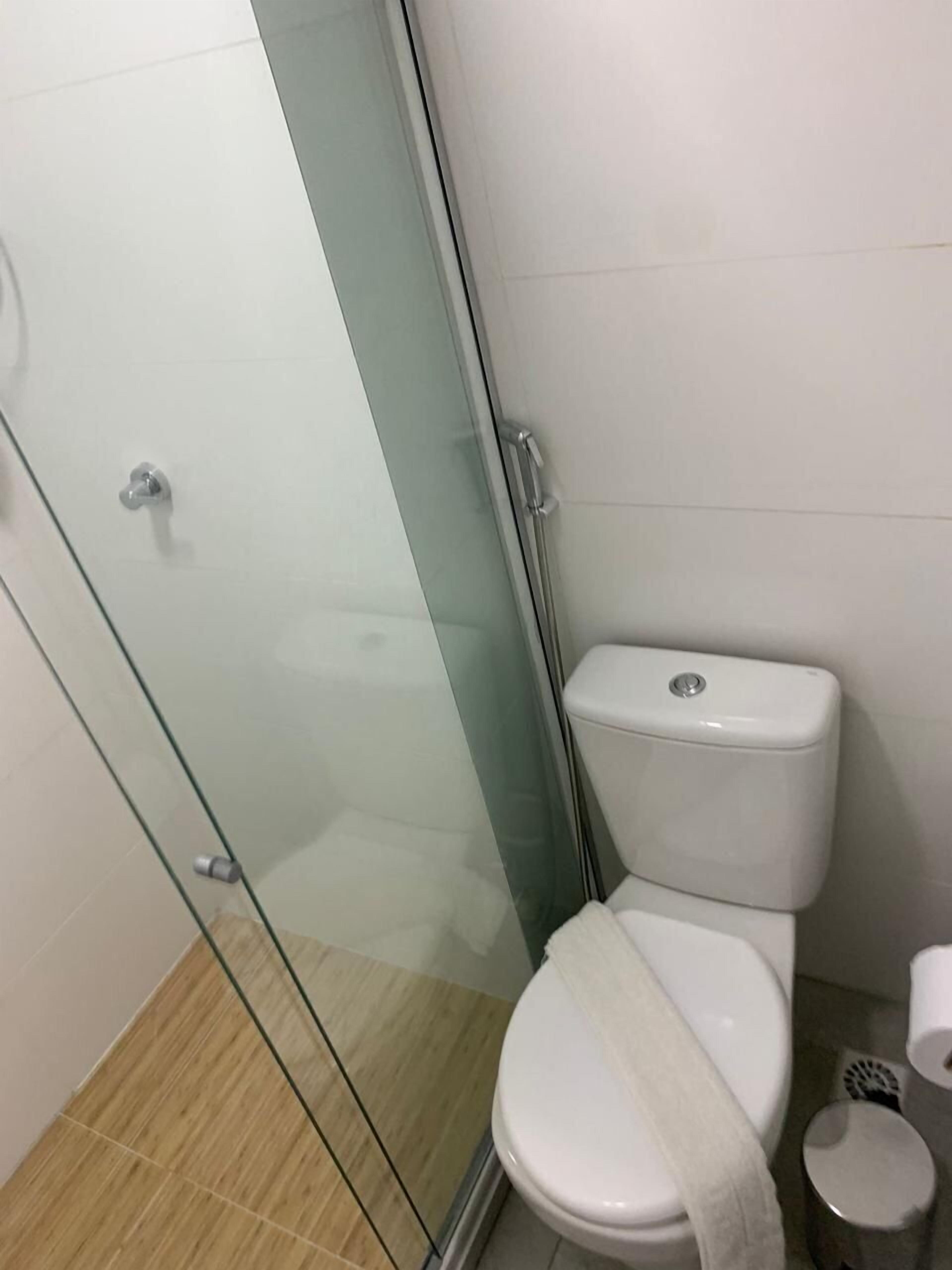 Ein Badezimmer mit Duschkabine aus Glas, einer weißen Toilette und einer kleinen Mülltonne.