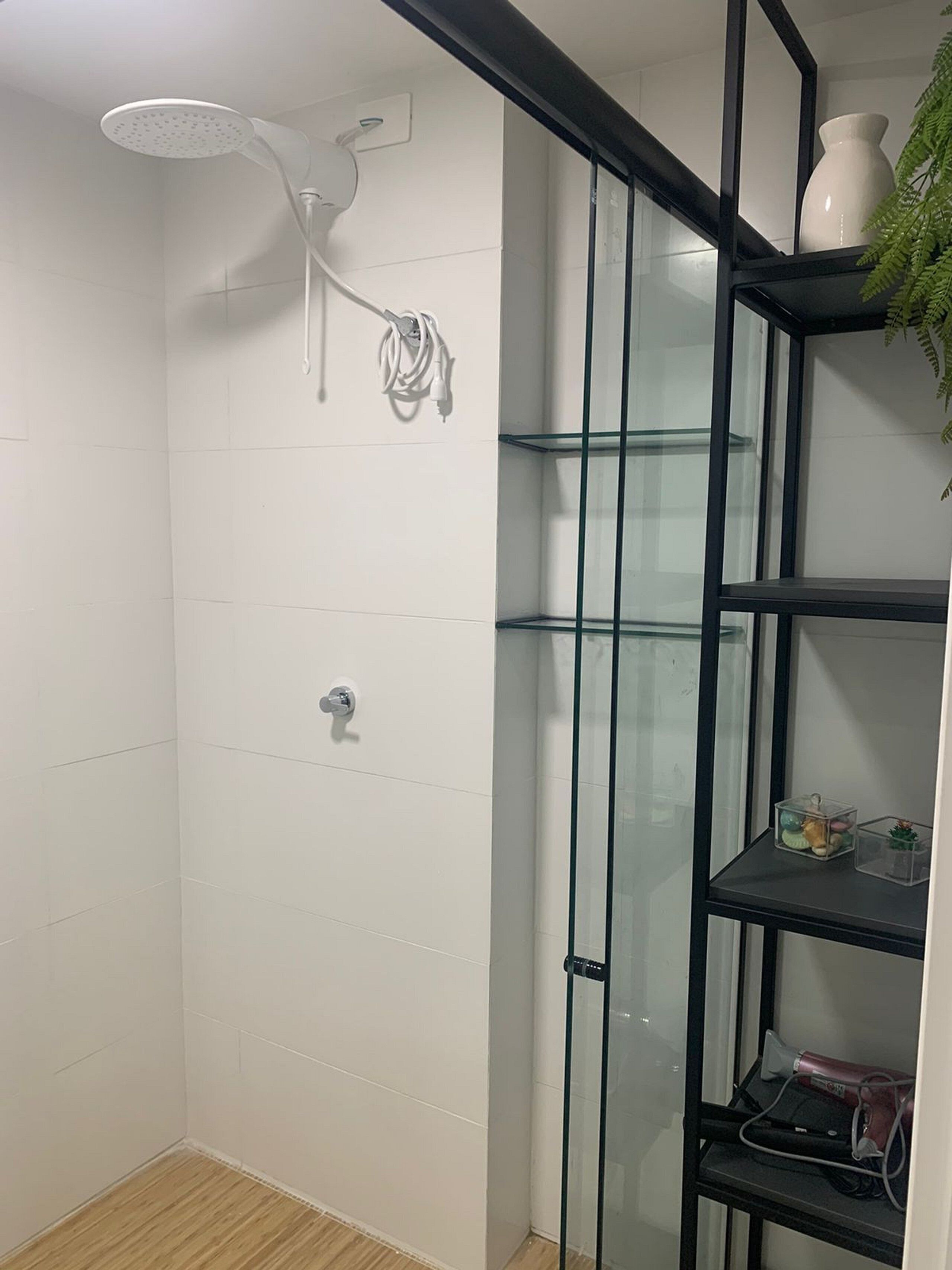 A shower with a handheld showerhead, a glass shelf unit with decorative items, and a potted plant.
