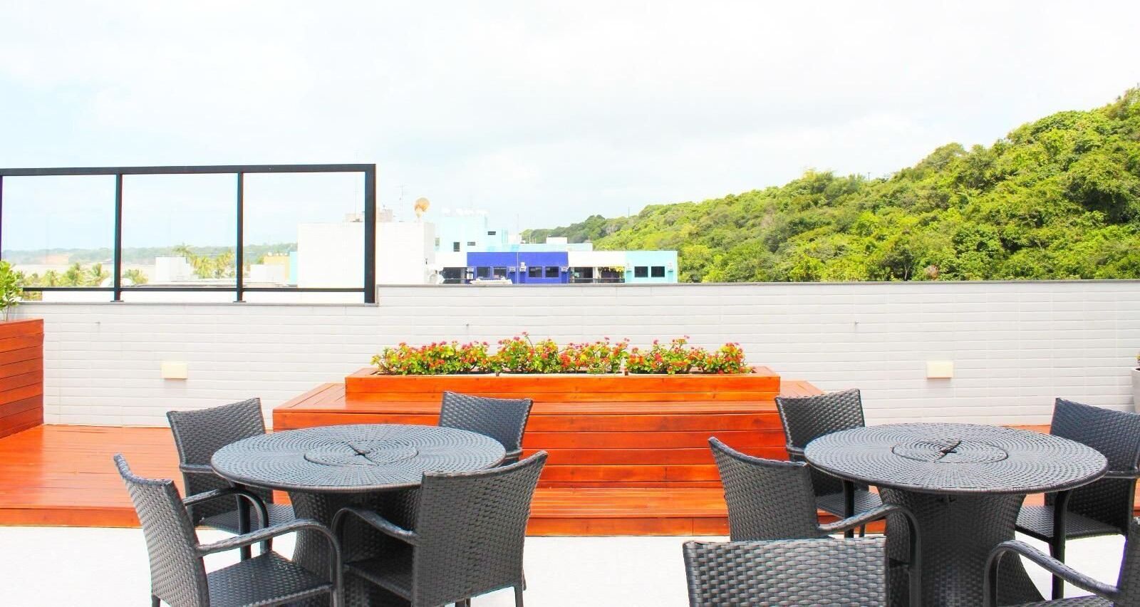 Eine Dachterrasse mit Korbtischen und -stühlen, einem Holzpflanzgefäß mit Blumen und Blick auf Gebäude und Grünflächen.