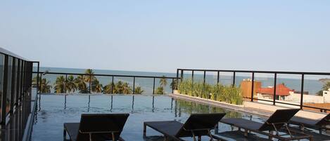 An infinity pool with lounge chairs, a view of the ocean, and palm trees.