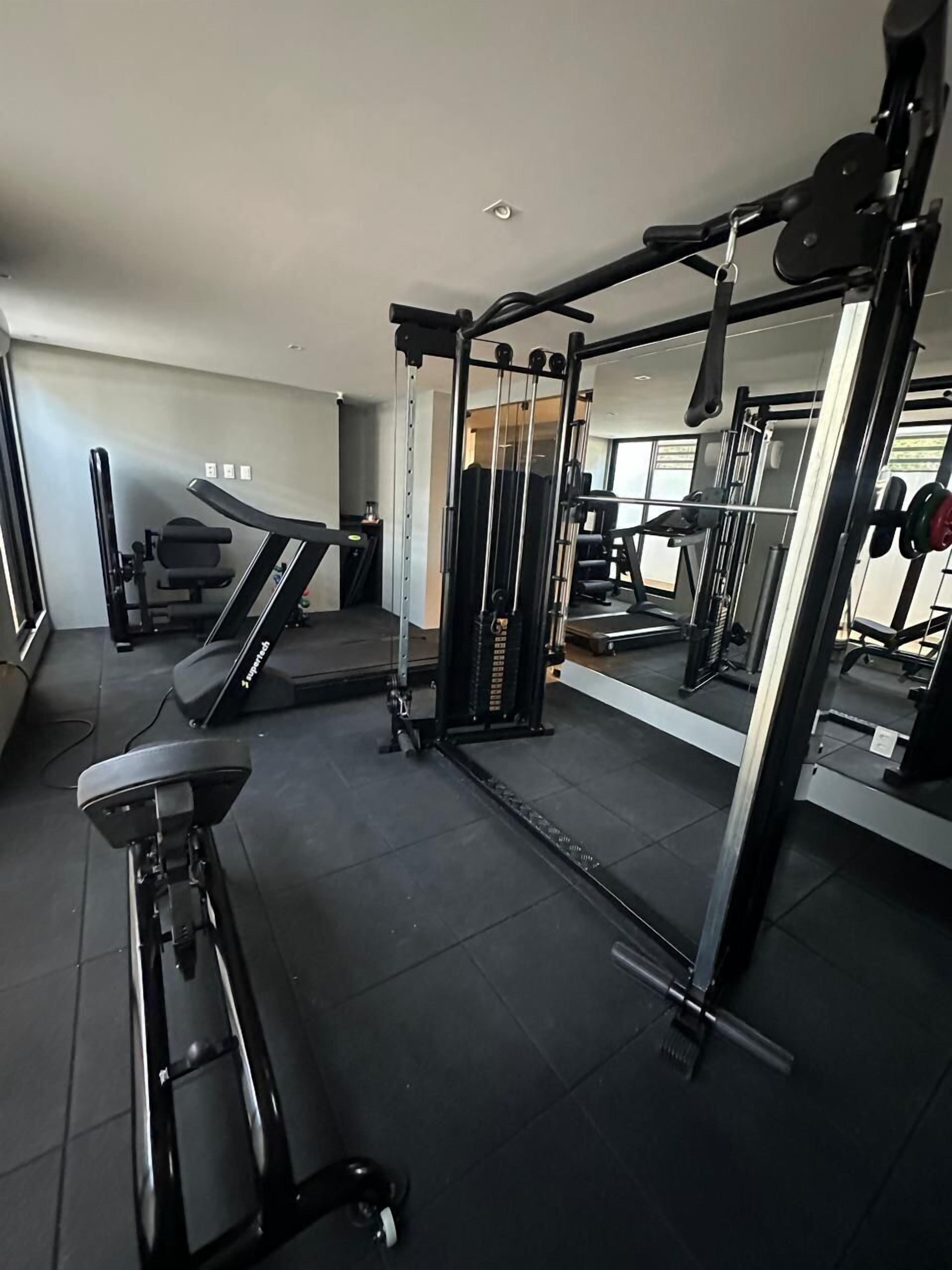 Un gimnasio con cinta de correr, máquinas de pesas y un espejo.