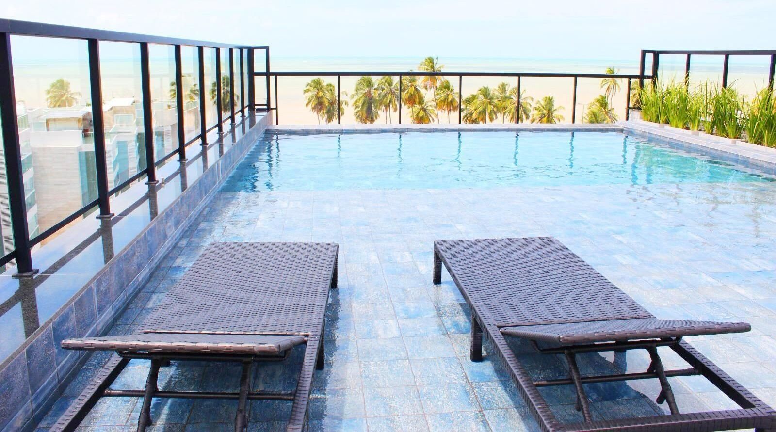 A rooftop infinity pool with two lounge chairs and a view of the beach.