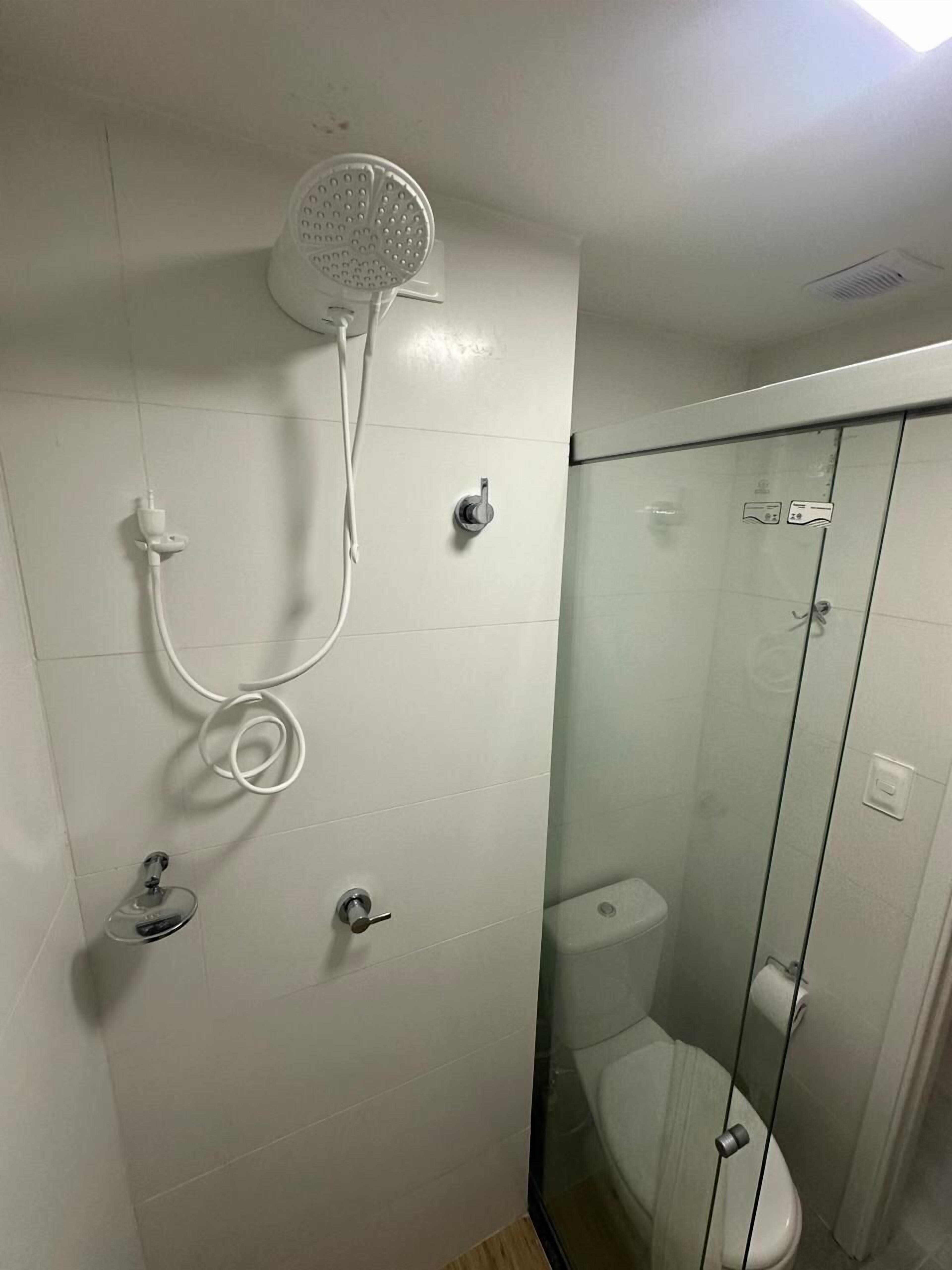 A small, enclosed shower area with a glass partition, a handheld showerhead, and a toilet.