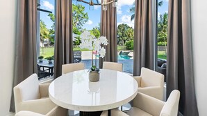 Une table ronde entourée de six chaises, un lustre et une vue sur une piscine et un espace verdoyant.