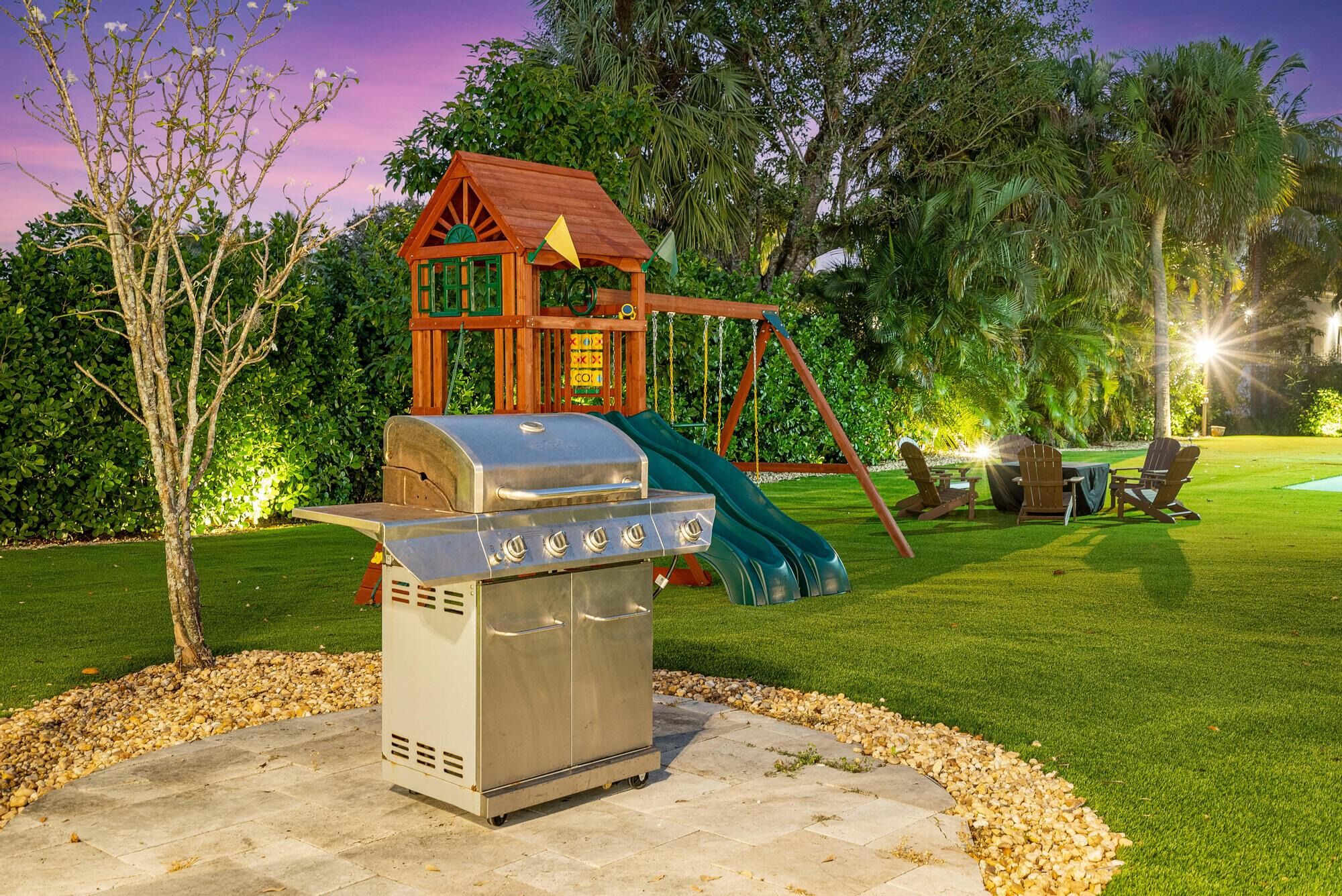 A backyard with a barbecue grill, a swing set, and outdoor seating.