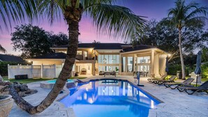 Une maison à deux étages avec une piscine, un espace salon extérieur et un jardin clôturé.