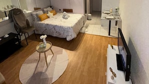 A compact bedroom with a bed, bedside table, chair, and a small round table with a lamp.