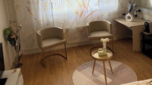 A modern room with two chairs, a small round table, a bed, a desk, and a large mirror.