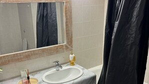 A bathroom with a white sink, a mirror, a black shower curtain, and a small bottle of soap on the counter.