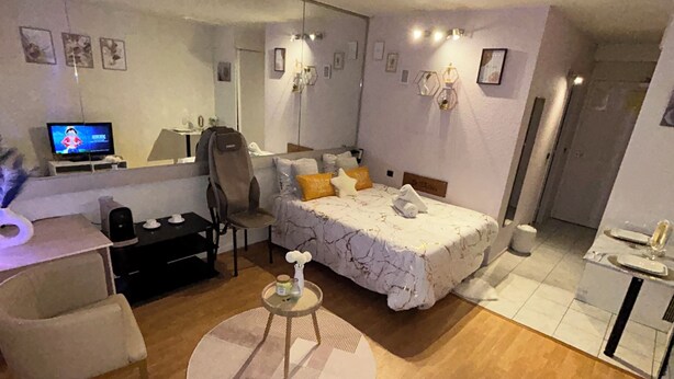 A modern hotel room with a large bed, a desk with a computer, a chair, and a small round table with a vase.