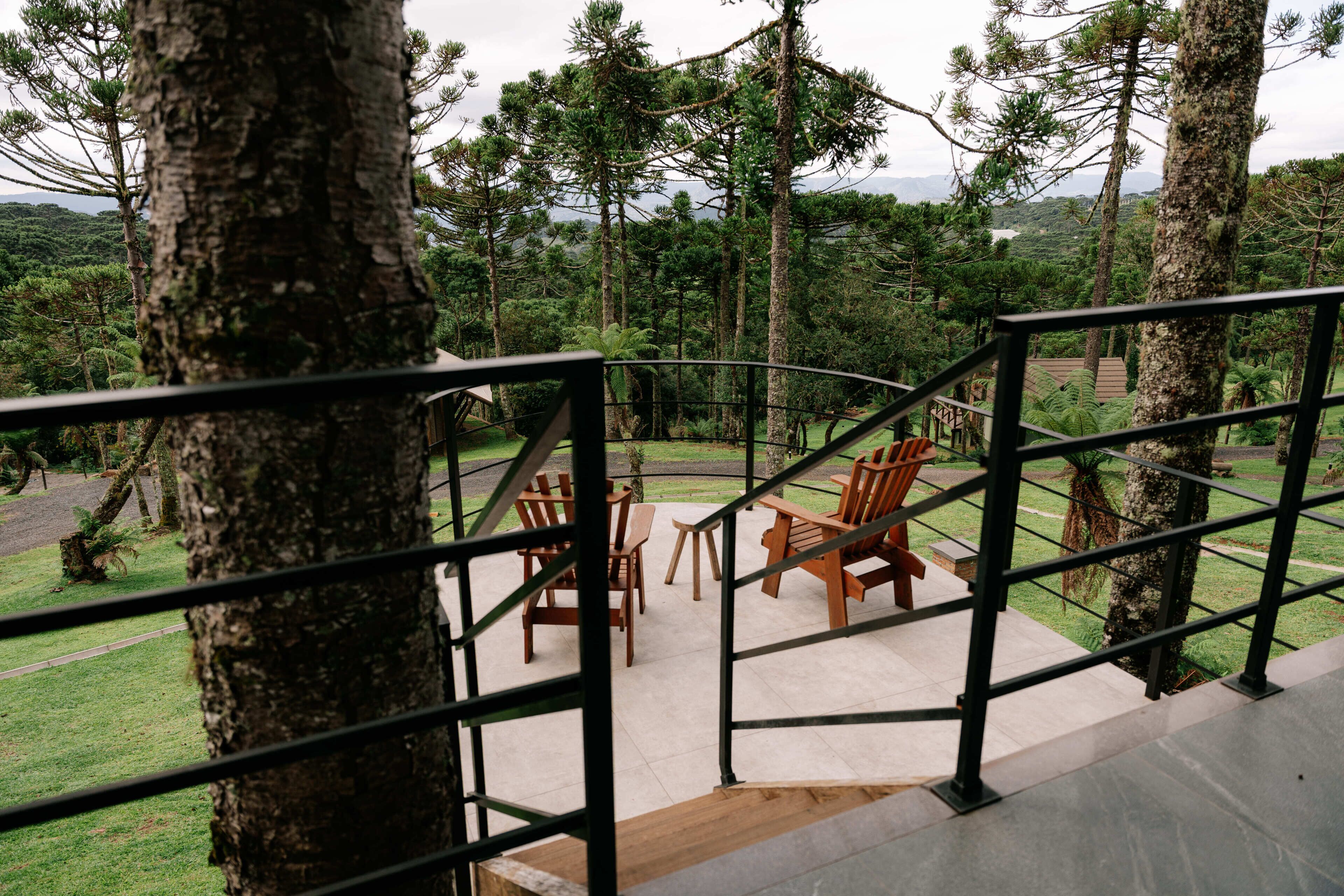 Un terrazzo in legno con sedie e un tavolo, immerso tra alberi e affacciato sul paesaggio.