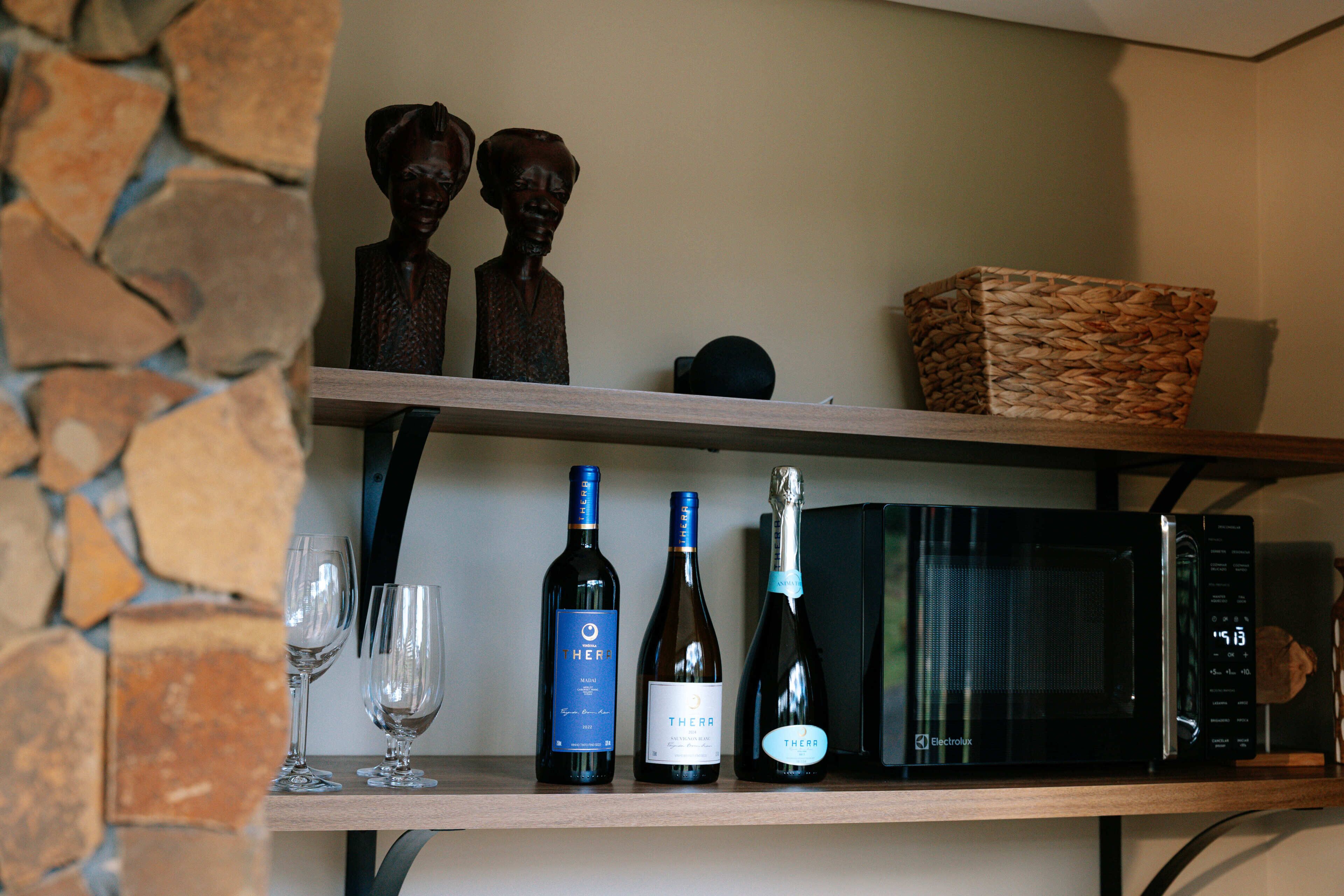 Uma prateleira com garrafas de vinho, copos e um micro-ondas.