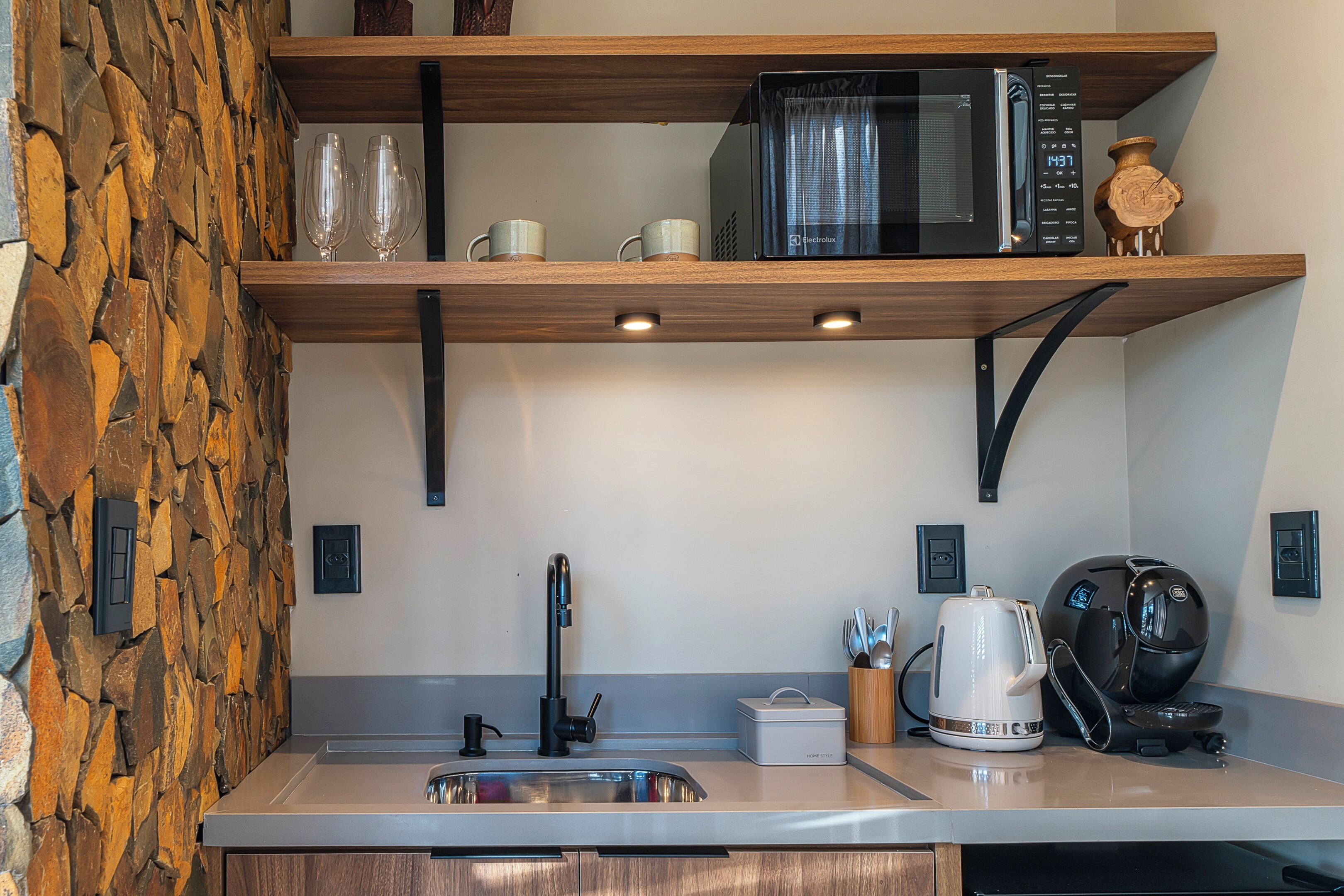 A kitchen with a stone wall, a sink, a microwave, and a coffee maker.