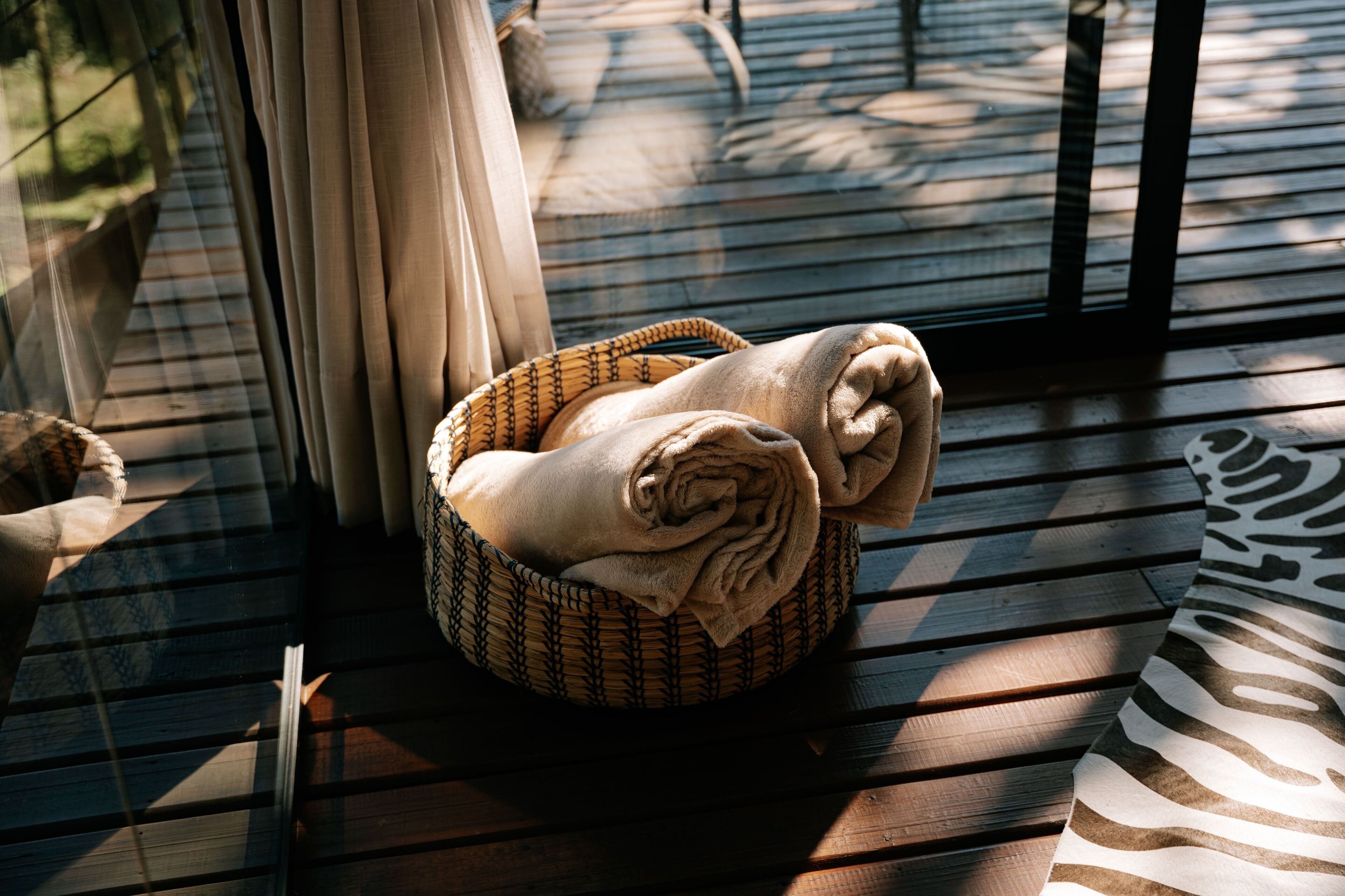 Eine Holzdielen-Terrasse mit einem gewebten Korb, der ein zusammenrolltes Handtuch enthält.