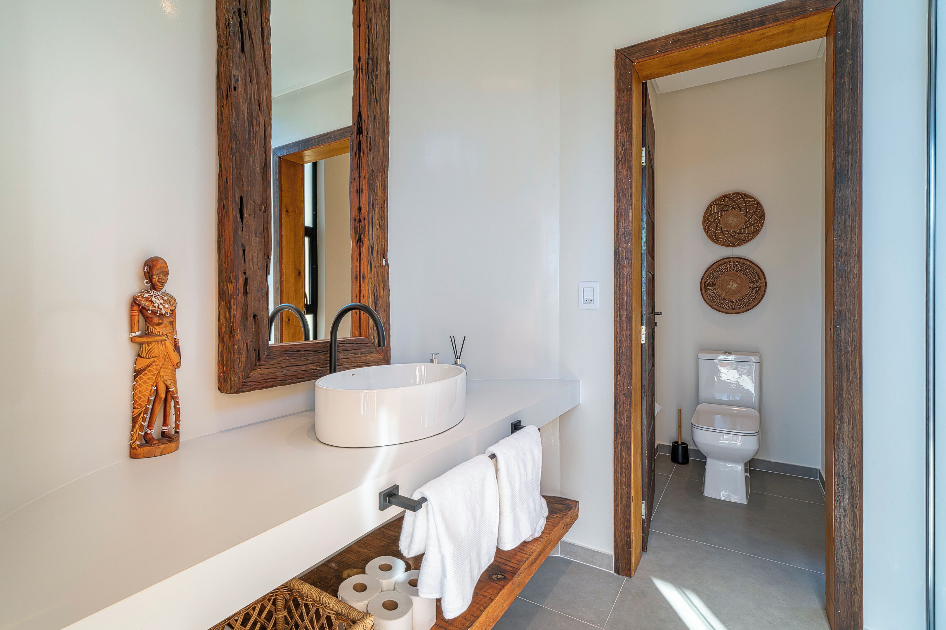 A modern bathroom with a wooden vanity, white sink, and a large mirror.