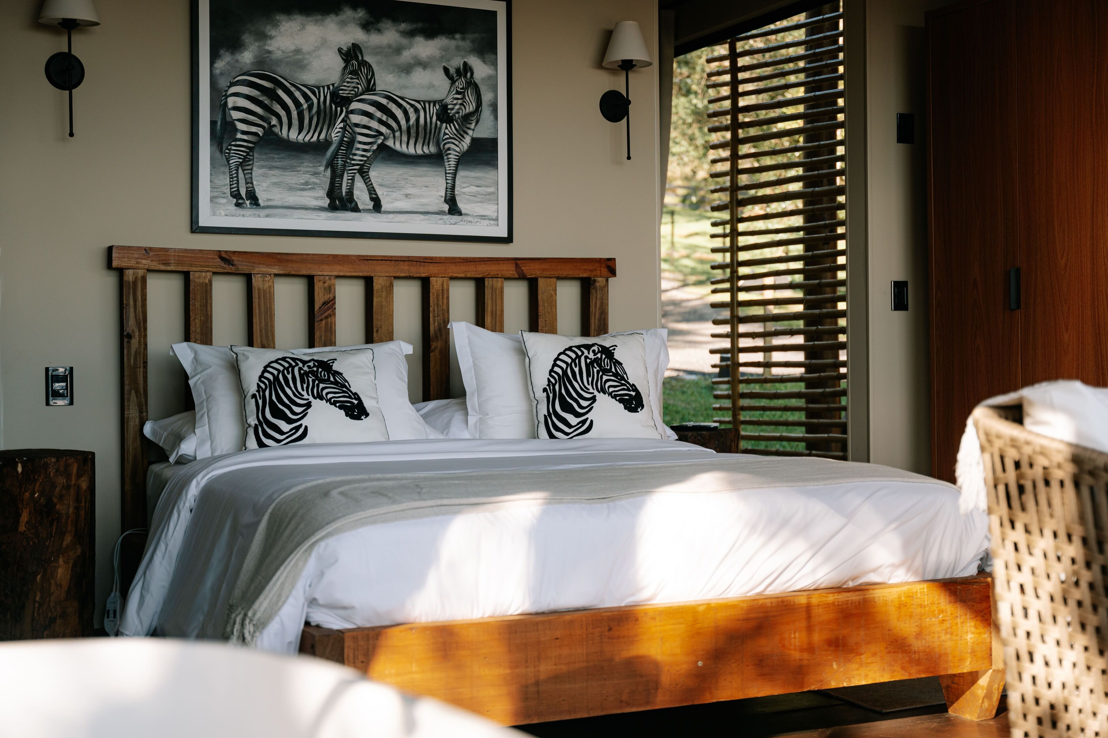 Een slaapkamer met een houten hoofdbord, wit beddengoed en kussens met zebraprint.