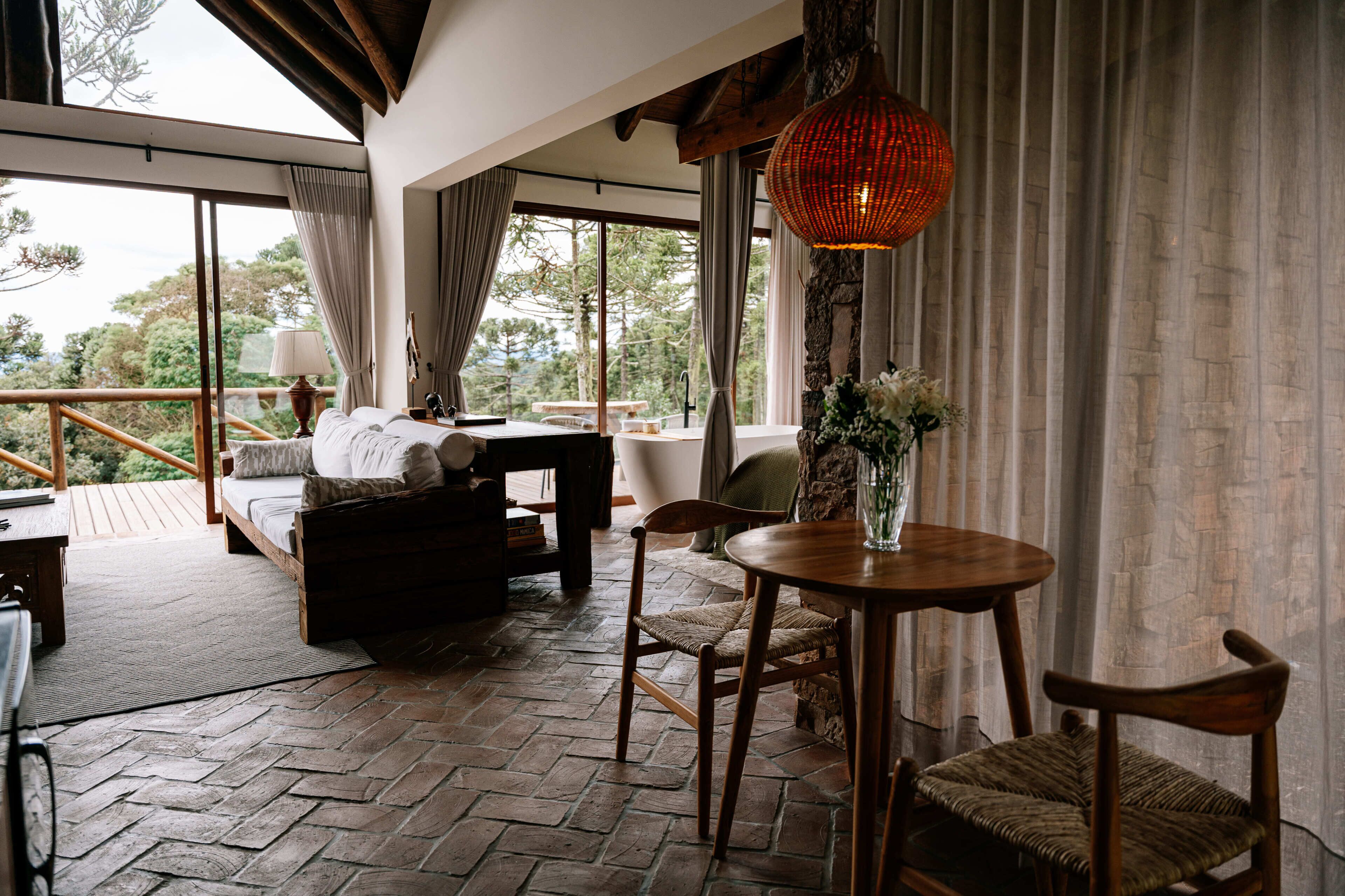 A cozy room with a bed, a table with chairs, a vase with flowers, and a large window with curtains.