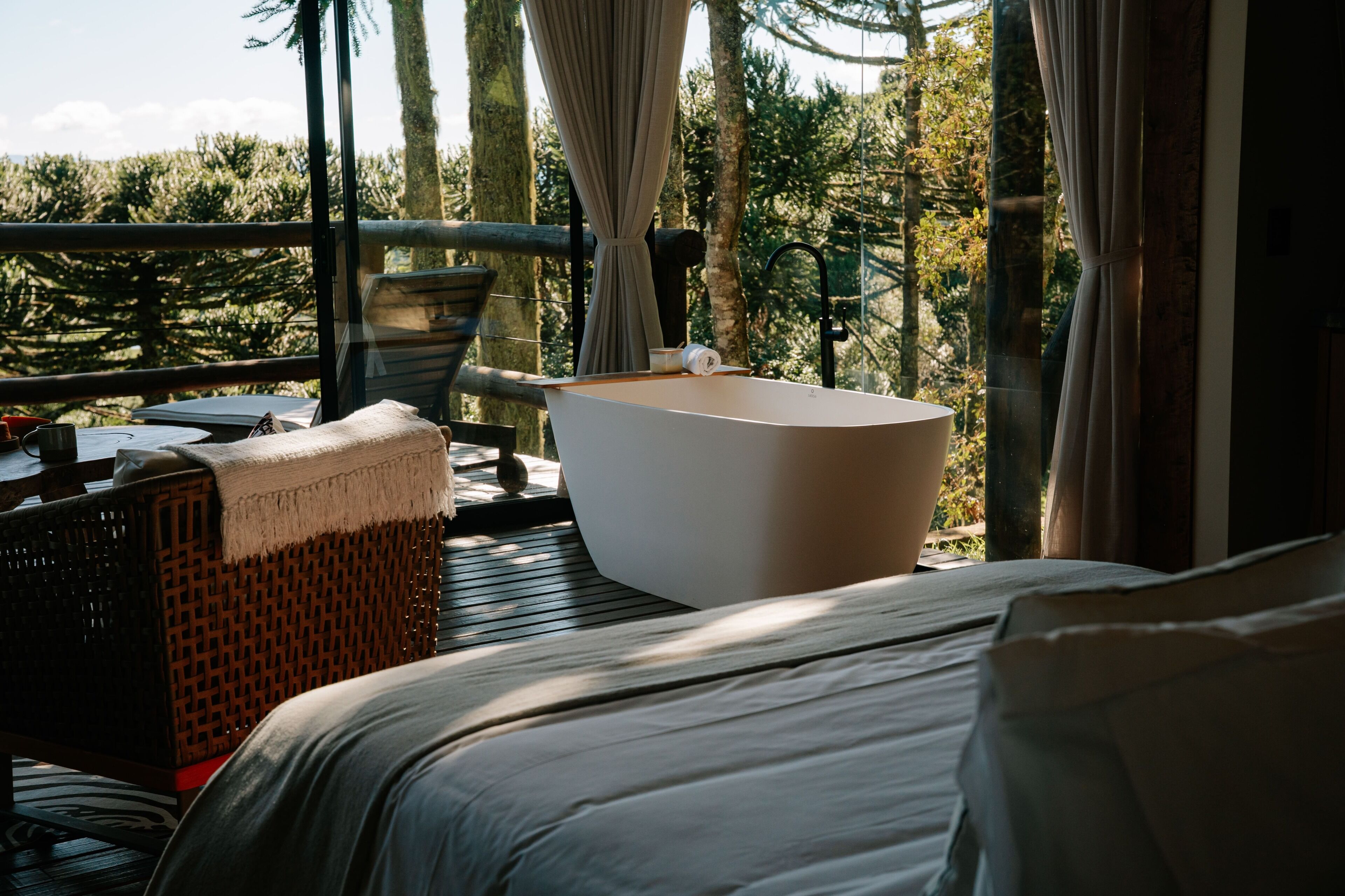 A bedroom with a large bed, a bathtub, and a view of trees.