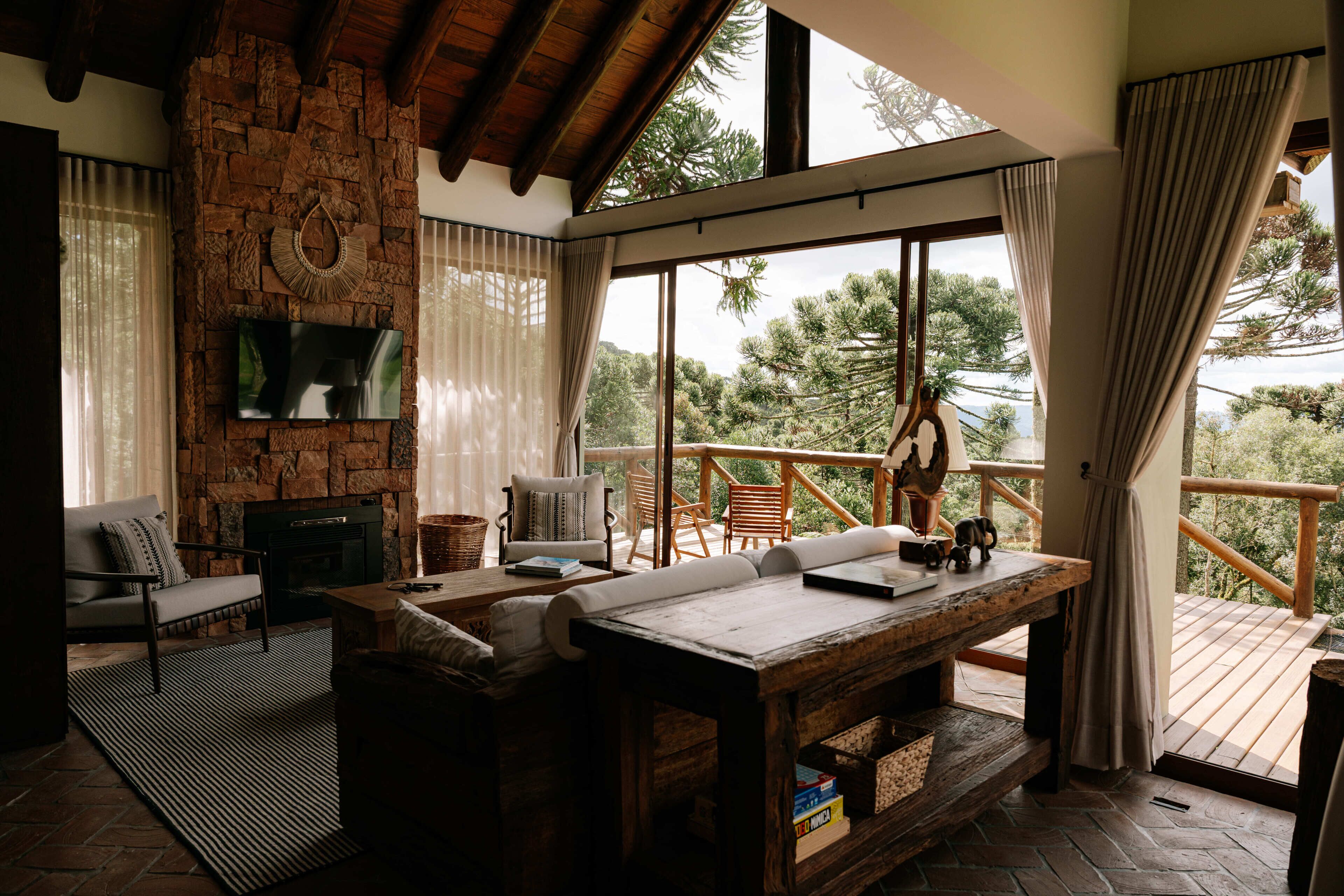 A cozy living area with a stone fireplace, comfortable seating, and a large window overlooking a forested landscape.