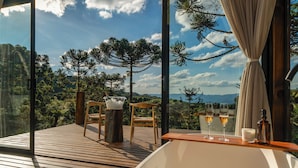 A balcony with wooden flooring, two wicker chairs, a small table with a glass bowl, and two glasses of wine. - Bulawayo Lodge (Urubici)