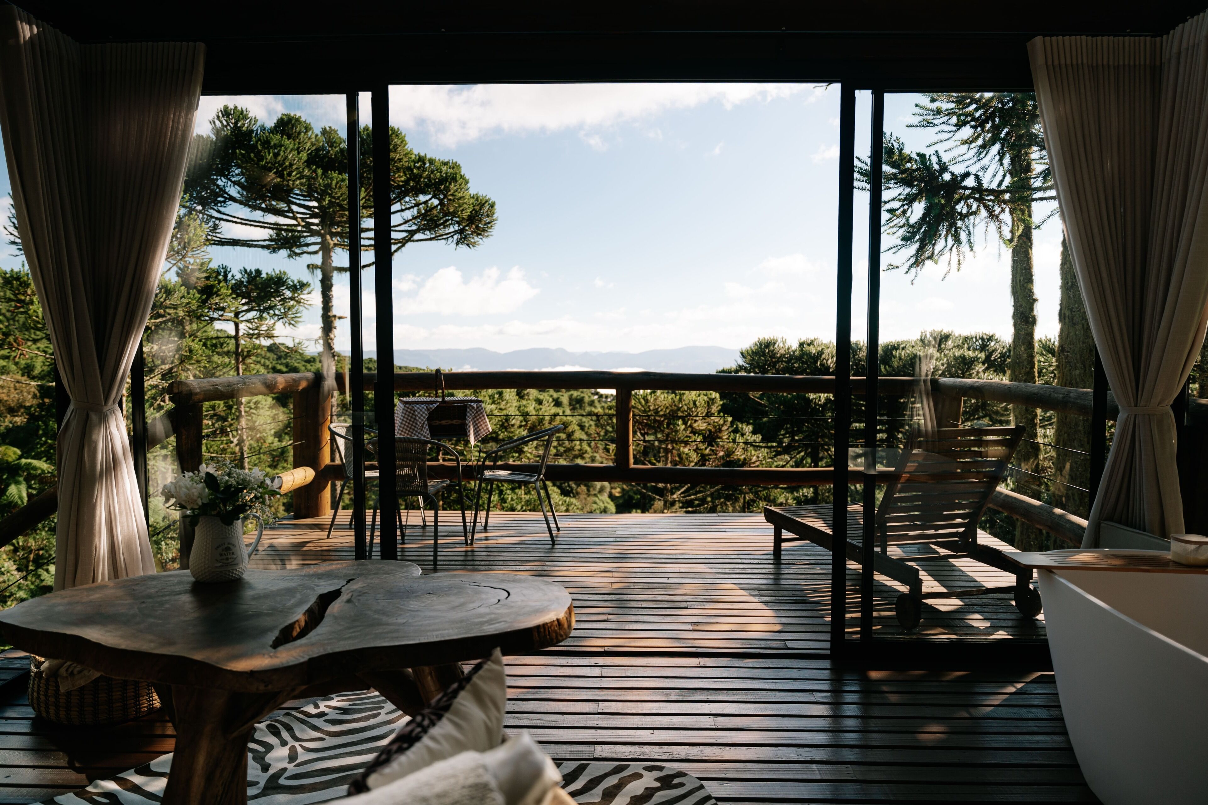 A wooden deck with a table and chairs, overlooking a forested landscape.