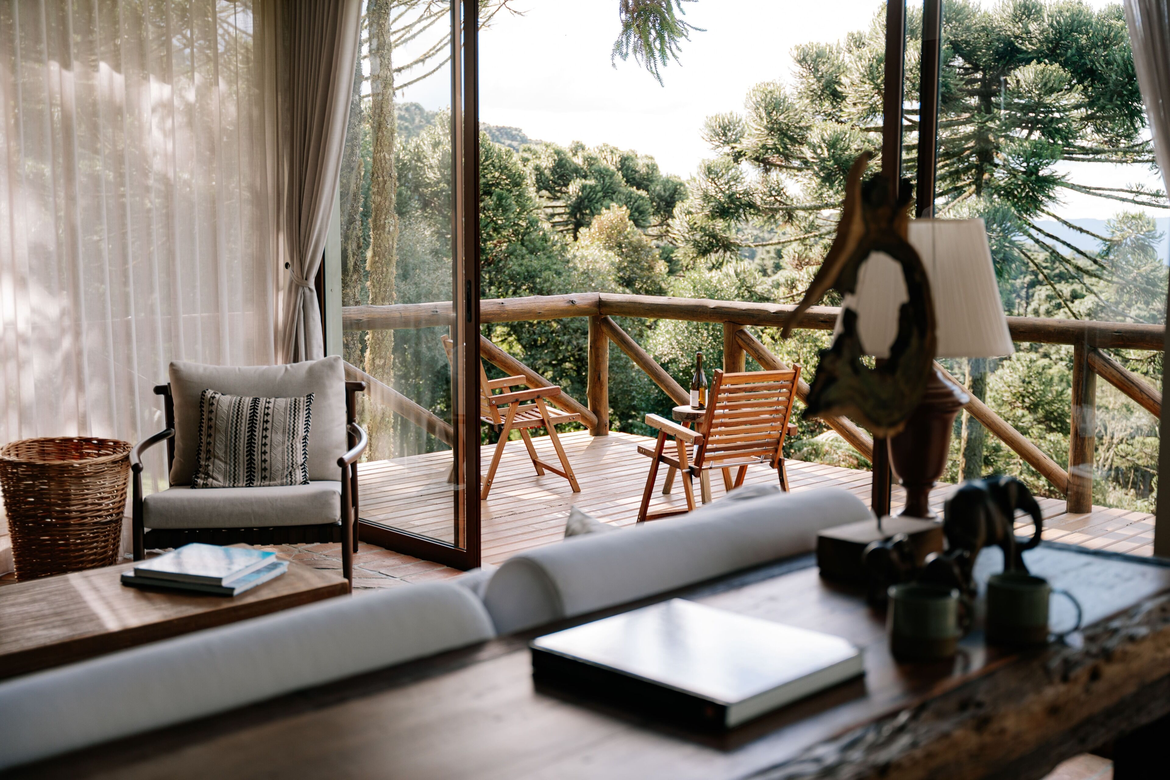 A cozy balcony with wooden furniture, a wicker basket, and a view of trees.
