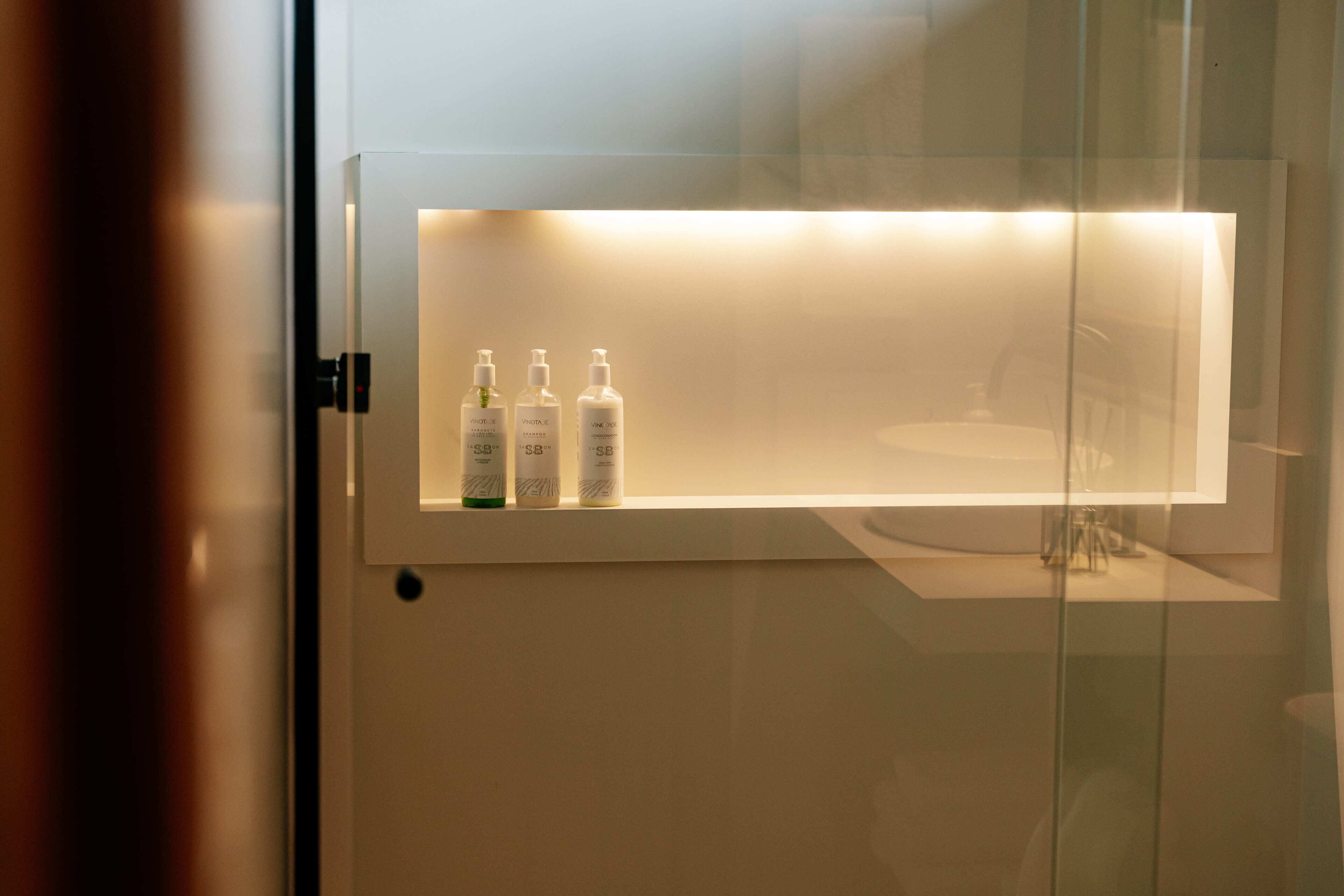 Et badeværelse med en hylde, hvor der står tre shampoo- og conditionerflasker.
