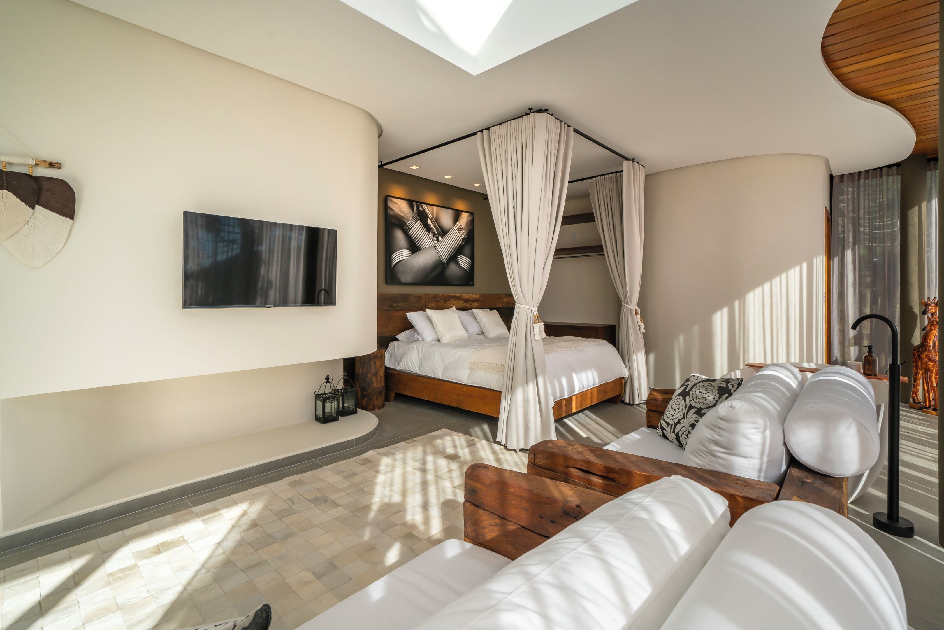 A bedroom with a canopy bed, a flat-screen TV, and a large window.
