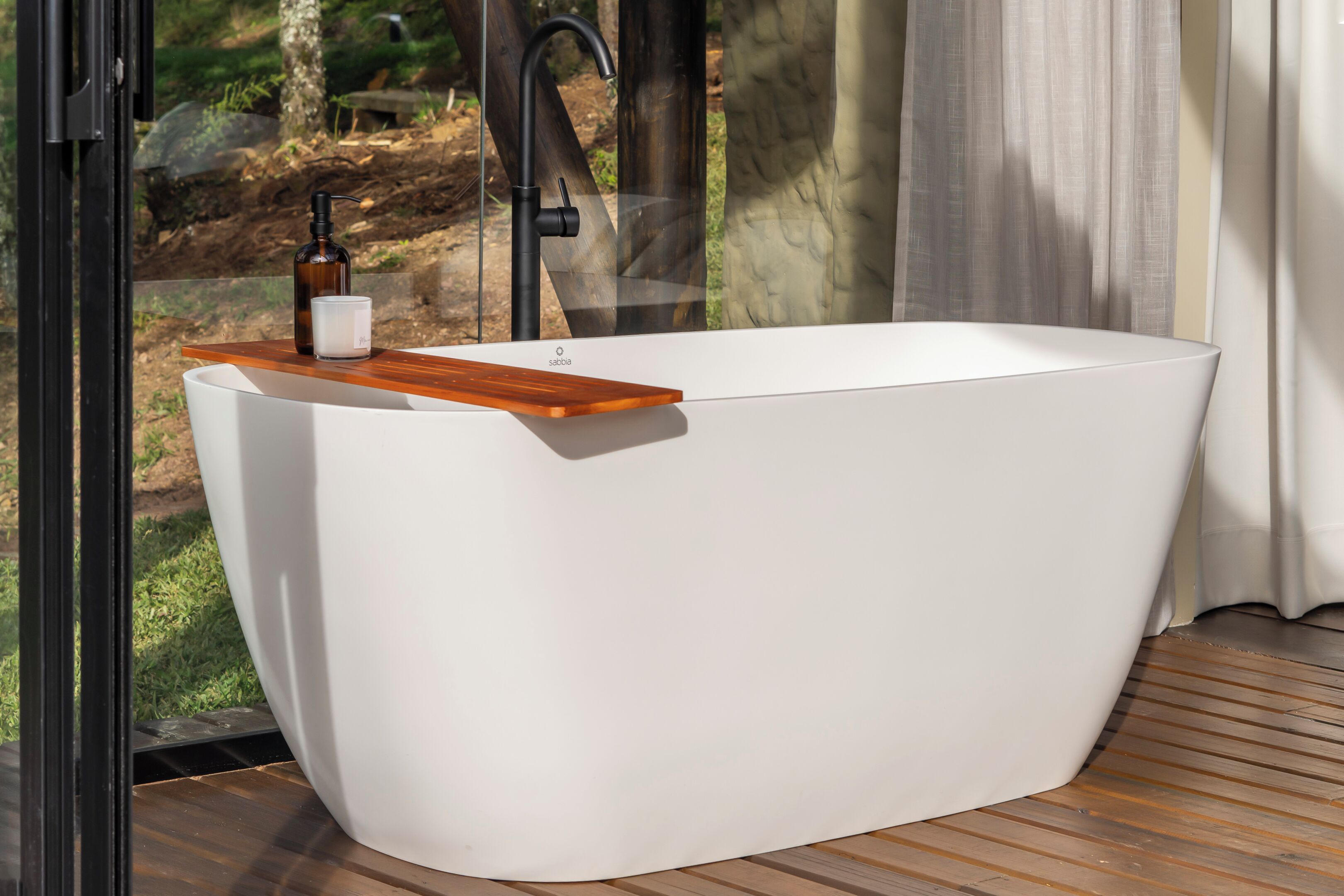 A modern bathroom with a freestanding bathtub, a wooden shelf, and a glass door leading to an outdoor area.