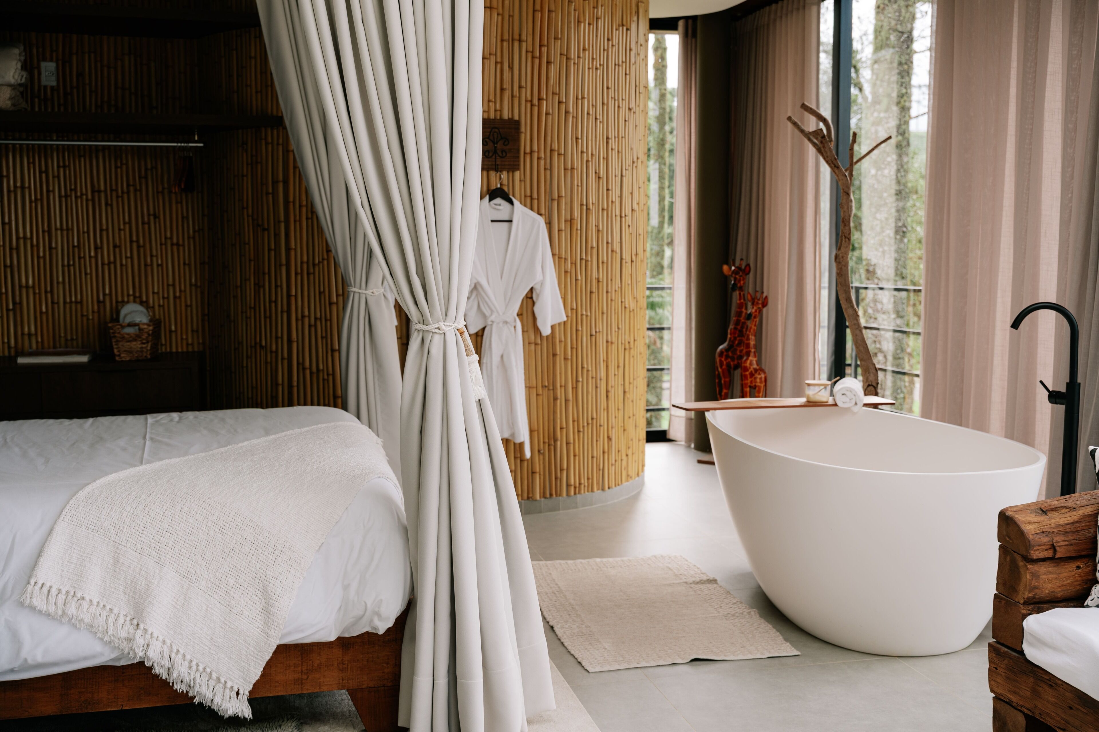 A modern bathroom with a freestanding bathtub, a wooden bath chair, and a large window with a view of trees.