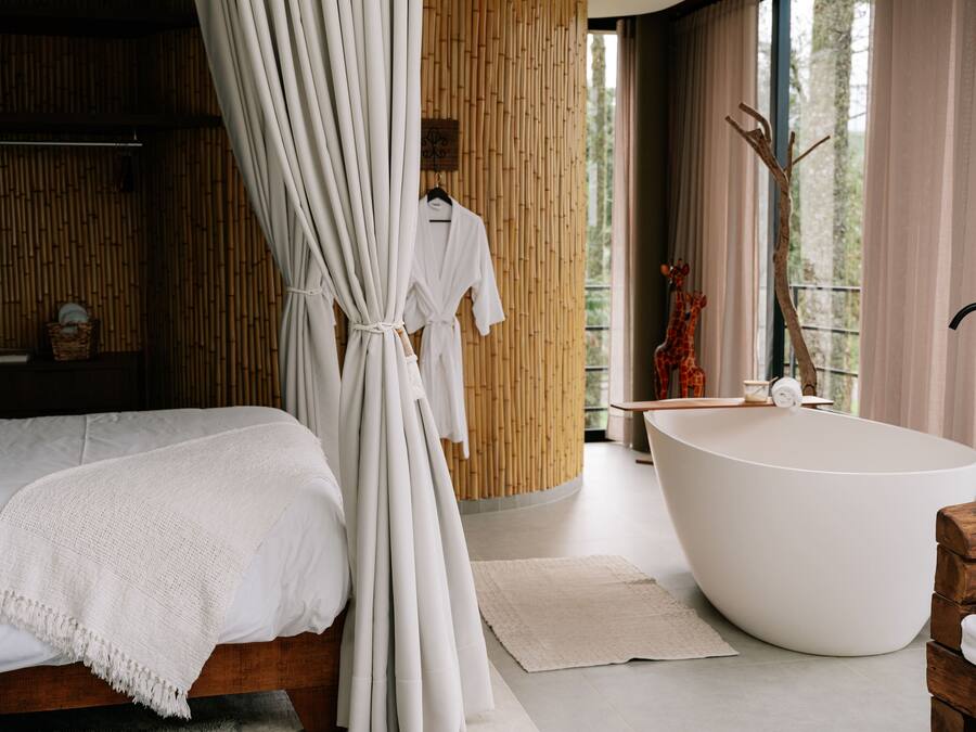 A modern bathroom with a freestanding bathtub, a wooden bath chair, and a large window with a view of trees.