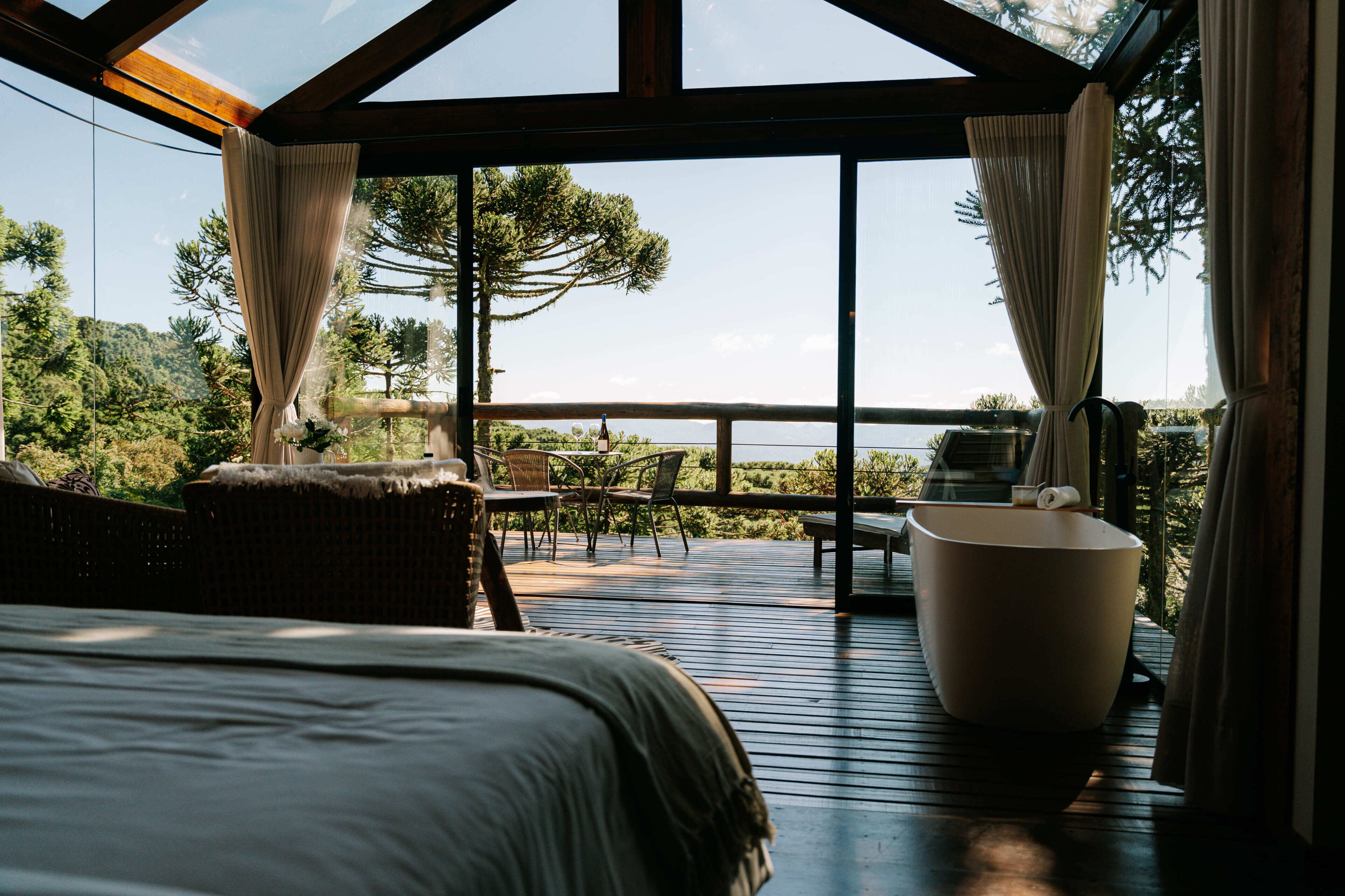 A bedroom with a large bed, a seating area with chairs, and a view of a mountainous landscape through large windows.