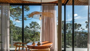 A modern room with a large window, a round wooden table, and two chairs. - Bulawayo Lodge (Urubici)