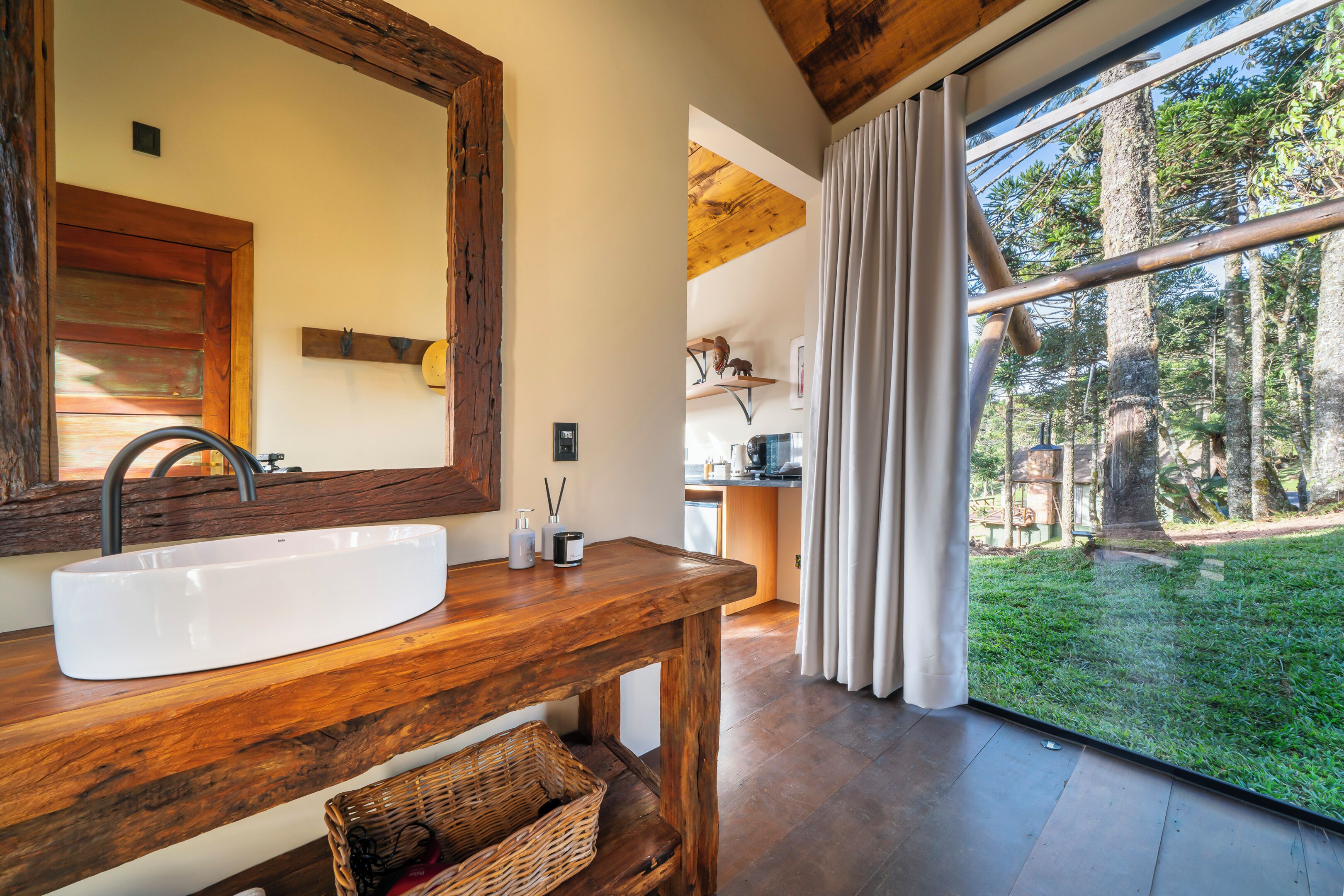 Une salle de bain avec un meuble-lavabo en bois, un grand miroir et une fenêtre donnant sur les arbres.