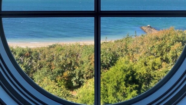 A circular window with a clear view of a beach and ocean. - Spacious 5-bedroom estate with access to private beach in peaceful Falmouth (Falmouth)