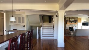 A spacious living area with a wooden floor, a dining area with a long table and chairs, a staircase, and a fireplace. - Spacious 5-bedroom estate with access to private beach in peaceful Falmouth (Falmouth)